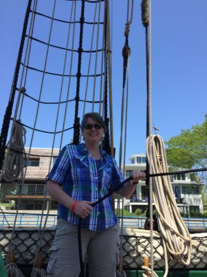 A woman in a plaid shirt holds a line on tall ship Friends Good Will