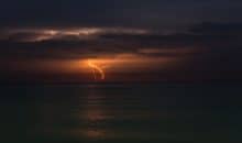 Lightning strikes in the distance over the ocean at night