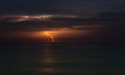 Lightning strikes in the distance over the ocean at night