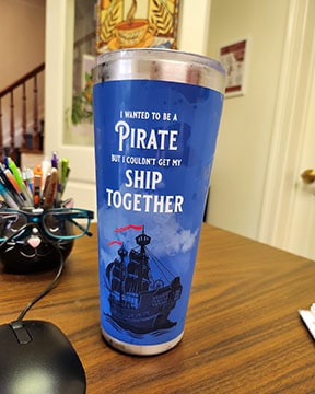A blue travel tumbler has an image of a tall ship on it. Text reads, "I wanted to be a pirate but I couldn't get my ship together"
